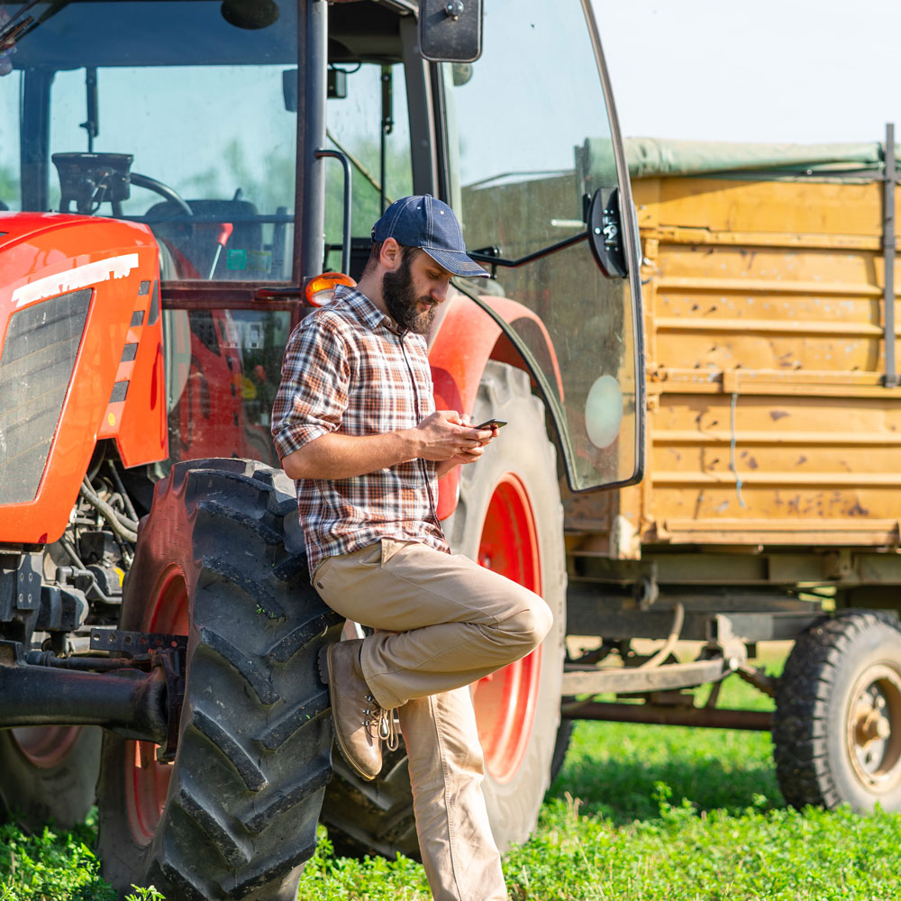 Stock image of a farmer, on his phone, leaning against his tractor