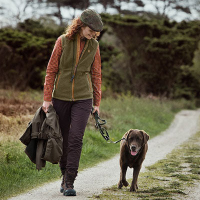 A woman walking a chocolate labrador dog